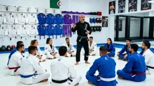 Entraînement de jiu jitsu en Algérie en 2025 avec un groupe de débutants et intermédiaires en kimono sur tatami dans un dojo moderne, coach algérien donnant des explications techniques.